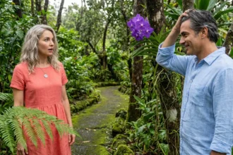 A man and woman reconnecting in a lush Hawaiian botanical garden, highlighting a silver compass pendant and a purple orchid.